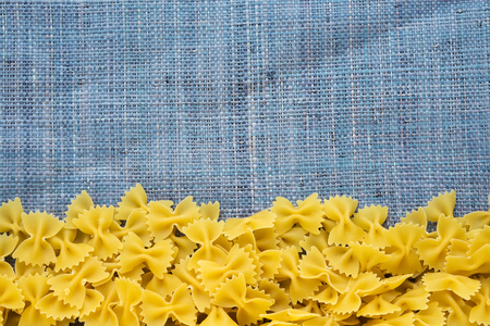 farfalle Raw farfallini Beautiful decomposed pasta with a bottom on a rustic blue knitted sack texture. Close-up view from the top. Free space for text.の写真素材