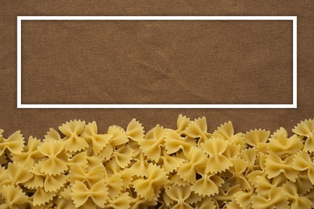 farfalle Raw farfallini Beautiful decomposed pasta from the bottom on a rustic brown textured background. Close-up view from the top. With white frame for text.の写真素材