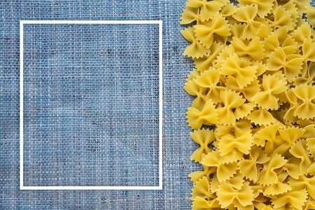 farfalle Raw farfallini Beautiful decomposed pasta with the right, on its side on a rustic blue knitted sack texture background. Close-up view from the top. With white frame for text.の写真素材