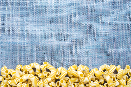 Raw cavatappi Beautiful decomposed pasta with a bottom on a rustic blue knitted sack texture. Close-up view from the top. Free space for text.の写真素材