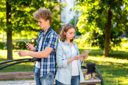 Young tourists guy with a girl. In the summer in the city in nature. In the hands holds a smartphone road map. The concept is lost. With gesture of hands choose the road.の写真素材