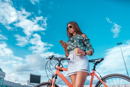 The girl in the summer in city, stands next to a red bicycle, in a white skirt and a green blouse....