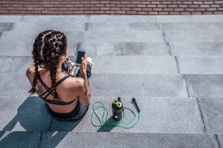 Girl with tattoos in sportswear, view from above, from behind. He holds a smartphone in his hands,...