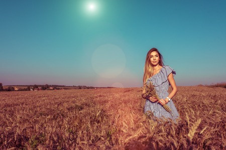 Girl in a wheat field in her hands holding ears of wheat. In the summer in the fresh air.の写真素材