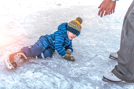 Little boy, 4-5 years old, winter uniform, blue overalls hat, fell on ice skates. The concept of...