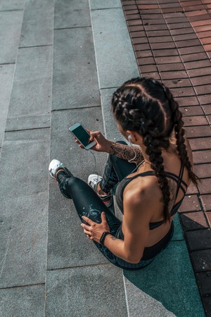 Girl athlete sitting steps resting after workout fitness summer city, day morning. Sportswear, smart phone, headphones. Active lifestyle, motivation power. Internet application music.の写真素材