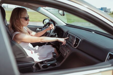 Girl driving a car, choosing navigation on monitor screen, presses touch menu, navigation map, route selection, online voice activation, assistant, touch menu activation on and offの写真素材