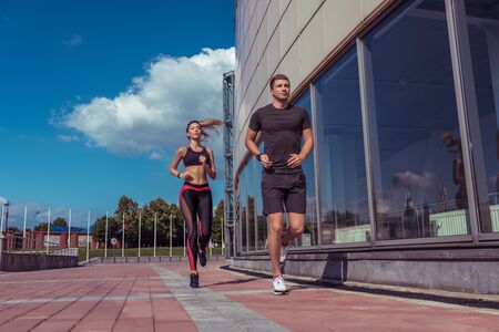 Athletic couple man and girl in summer city, run on morning run, burning calories, cardio fitness training day and morning. Healthy lifestyle style. Sportswear, friends and relationships are pairedの写真素材
