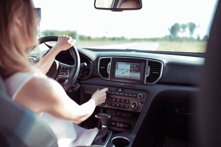 woman driving car, summer outside city, increases volume on radio, touch screen, automatic transmission, radio station selection, mechanical adjustment of air conditioner levelの写真素材