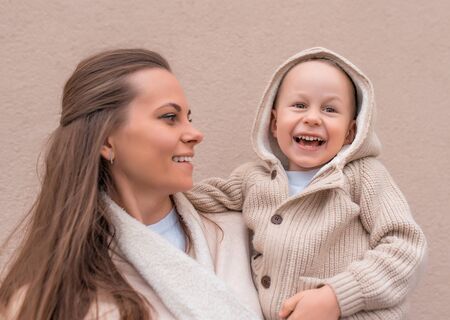 happy and young family, woman, mother holds little boy in her arms, happy smiling couple having fun, warm autumn clothes with hood. Emotions of comfort, joy of holiday care of loveの写真素材