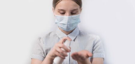 teenager girl of 13-14 years old, in medical mask covers face, holds an antiseptic spray in hand, disinfects hands from viruses bacteria, COVID-19 epidemic pandemic virus outbreak protection concept.の写真素材