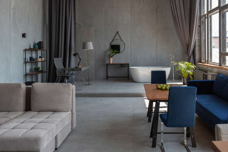 Modern minimalistic dark gray loft style studio apartment interior design. kitchen, sitting area, workplace, shower and bath. bright sun rays inside.の写真素材