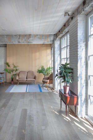 sitting room interior in loft style with huge windows and ordinary furniture. armchair and sofa. sun...