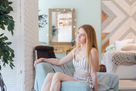gorgeous blonde lady in fashionable spacious apartment with a stylish design in green, gray and white pastel colors with big window and decorative wallsの写真素材