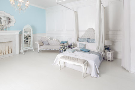 bright, clean stylish interior bedroom and living room with a large panoramic window. beautiful rich antique furniture. four-poster bed, a mirror and a sofa.の写真素材