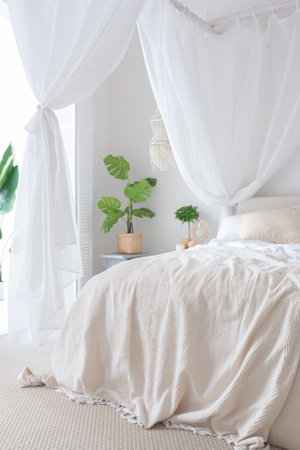 Cozy interior of a bright Balinese-style apartment with white walls, bamboo furniture. bed room with night lights, bed with balanchin and large windowsの写真素材