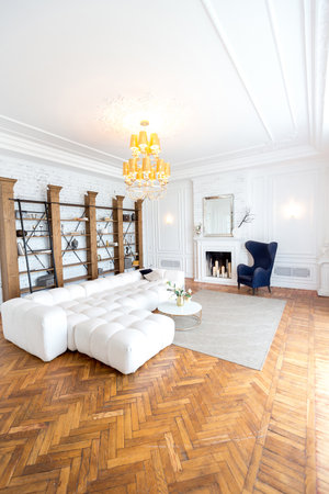 modern interior of a luxurious large bright living room. white expensive sofa and wooden shelving, white walls with moldings and a luxurious chandelierの写真素材
