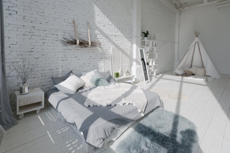 Spacious stylish modern trendy loft apartment in white and light colors. a large room full of sunlight. brick wall, wood floor, shelving, pallet bed and teepee-shaped children's house. everything is white with gray tints.の写真素材