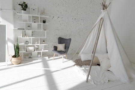 Spacious stylish modern trendy loft apartment in white and light colors. a large room full of sunlight. brick wall, wood floor, shelving, pallet bed and teepee-shaped children's house. everything is white with gray tints.の写真素材
