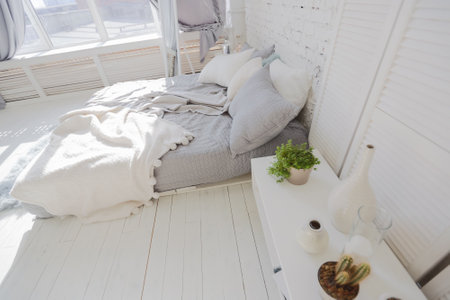 Spacious stylish modern trendy loft apartment in white and light colors. a large room full of sunlight. brick wall, wood floor, shelving, pallet bed and huge window. everything is white with gray tints.の写真素材