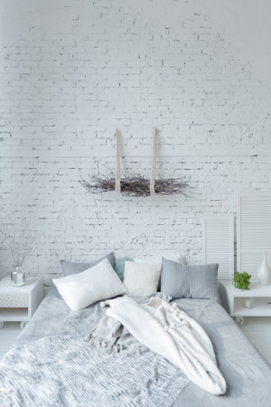 Spacious stylish modern trendy loft apartment in white and light colors. a large room full of sunlight. brick wall, wood floor, shelving, pallet bed and huge window. everything is white with gray tints.の写真素材