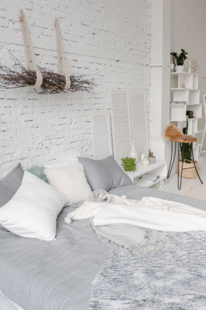 Spacious stylish modern trendy loft apartment in white and light colors. a large room full of sunlight. brick wall, wood floor, shelving, pallet bed and huge window. everything is white with gray tints.の写真素材