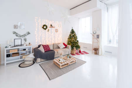 large very bright spacious stylish open plan Bali style apartment with hanging bed and panoramic windows. white floor and walls, simple wooden furniture. decorated with a christmas treeの写真素材