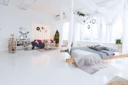 large very bright spacious stylish open plan Bali style apartment with hanging bed and panoramic windows. white floor and walls, simple wooden furniture. decorated with a christmas treeの写真素材