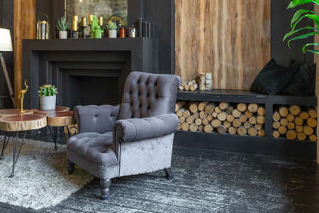dark brutal interior of sitting room decorated with wooden logs. yellow and gray soft armchairs, huge arc window and fireplaceの写真素材