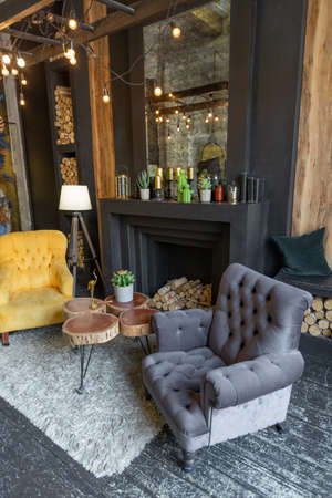 dark brutal interior of sitting room decorated with wooden logs. yellow and gray soft armchairs,...