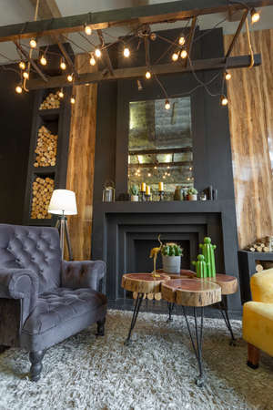dark brutal interior of sitting room decorated with wooden logs. yellow and gray soft armchairs,...