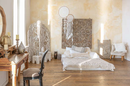 modern interior of a bright room in a two-storey apartment with decorative items in bali style with a balcony. white walls, wood floors and vintage furnitureの写真素材