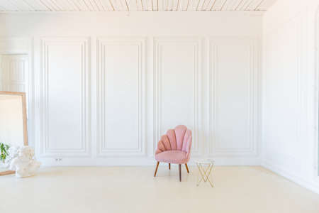 delicate and cozy light interior of the living room with modern stylish furniture of pastel pink color and white walls with stucco moldings in daylightの写真素材