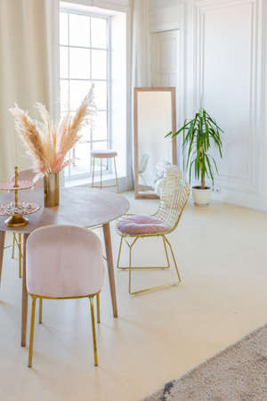 delicate and cozy light interior of the living room with modern stylish furniture of pastel pink color and white walls with stucco moldings in daylightの写真素材