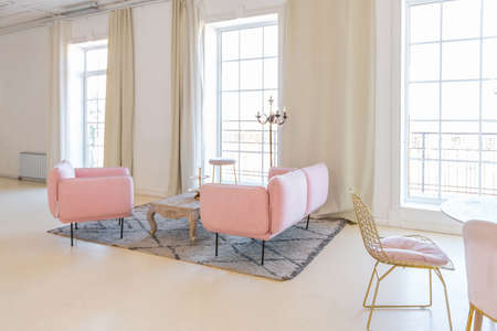 delicate and cozy light interior of the living room with modern stylish furniture of pastel pink color and white walls with stucco moldings in daylightの写真素材