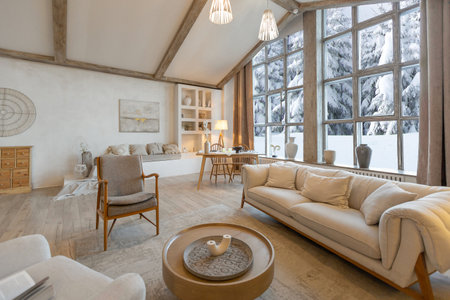 cozy warm home interior of a chic country chalet with a huge panoramic window overlooking the winter forest. open plan, wood decoration, warm colors and a family hearthの写真素材