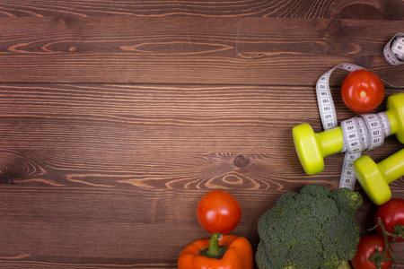 Fitness concept with dumbbells, measuring tape and vegetables on wooden backgroundの写真素材