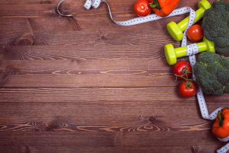 Fitness background with dumbbells, fresh vegetables and measuring tape on wooden boardの写真素材