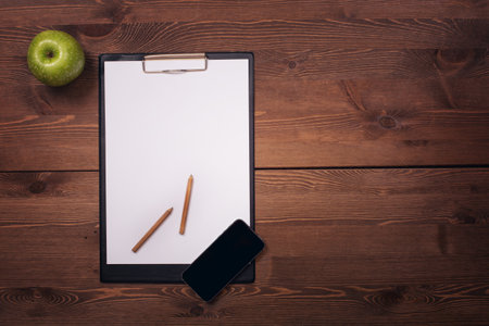 Blank clipboard with pencils and smartphone on wooden table. Top viewの写真素材