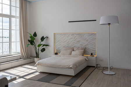 bedroom area in a minimalistic modern luxury design of an expensive house on a sunny day. decorative panel in the headboard, white walls with plaster, parquet, decorative lighting and no oneの写真素材