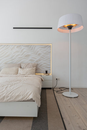 bedroom area in a minimalistic modern luxury design of an expensive house on a sunny day. decorative panel in the headboard, white walls with plaster, parquet, decorative lighting and no oneの写真素材