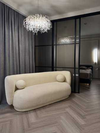A contemporary living area features a plush, rounded sofa with stunning chandelier lighting. The muted color scheme and sleek lines create an inviting atmosphere.の写真素材