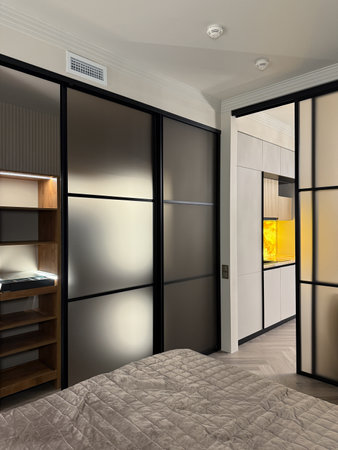 This cozy bedroom features a plush bed adorned with soft pillows, complemented by a sleek, modern closet illuminated from within, enhancing the room's ambiance and elegance.の写真素材