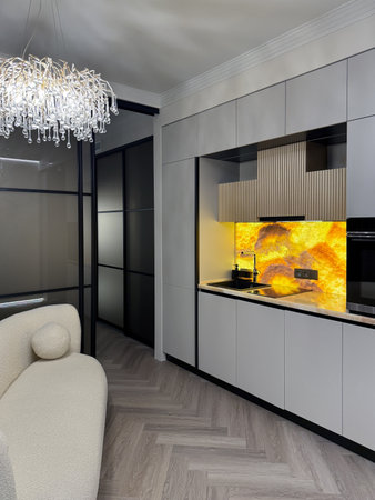 A stylish kitchen features minimalist cabinetry and a bright yellow backsplash, creating a vibrant focal point in a modern apartment. The open layout enhances the space's functionality and appeal.の写真素材