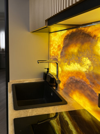 A stylish kitchen features minimalist cabinetry and a bright yellow backsplash, creating a vibrant focal point in a modern apartment. The open layout enhances the space's functionality and appeal.の写真素材