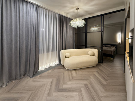 A contemporary living area features a plush, rounded sofa with stunning chandelier lighting. The muted color scheme and sleek lines create an inviting atmosphere.の写真素材