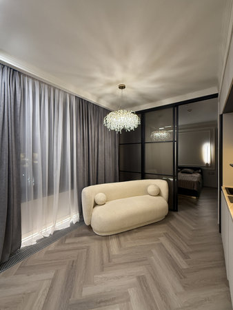 A contemporary living area features a plush, rounded sofa with stunning chandelier lighting. The muted color scheme and sleek lines create an inviting atmosphere.の写真素材