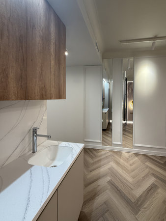 A contemporary apartment interior showcases a spacious layout with sleek wooden flooring and modern lighting fixtures. The kitchen area features minimalist cabinetry for a clean look.の写真素材