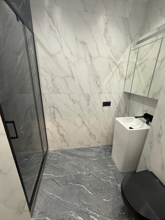 A chic bathroom showcases marble walls and a sleek design. Soft lighting highlights the details, while towels hang neatly by the shower, enhancing the sophisticated atmosphere.の写真素材