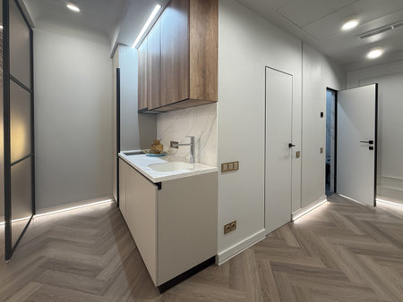 A contemporary apartment interior showcases a spacious layout with sleek wooden flooring and modern lighting fixtures. The kitchen area features minimalist cabinetry for a clean look.の写真素材